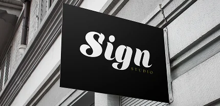 Black rectangular storefront sign mounted on a gray building facade, featuring the words “Sign Studio” in stylish white and olive-green font.