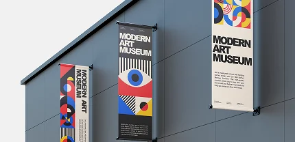 Three colorful vertical banners mounted on the exterior wall of a building, all promoting the Modern Art Museum. Each banner features abstract geometric designs and bold typography, with one prominently displaying an eye graphic.