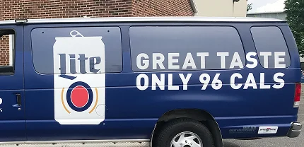 Blue delivery van with a large graphic of a Miller Lite beer can and bold white text that reads “GREAT TASTE ONLY 96 CALS.” The design promotes the low-calorie content of the beverage.