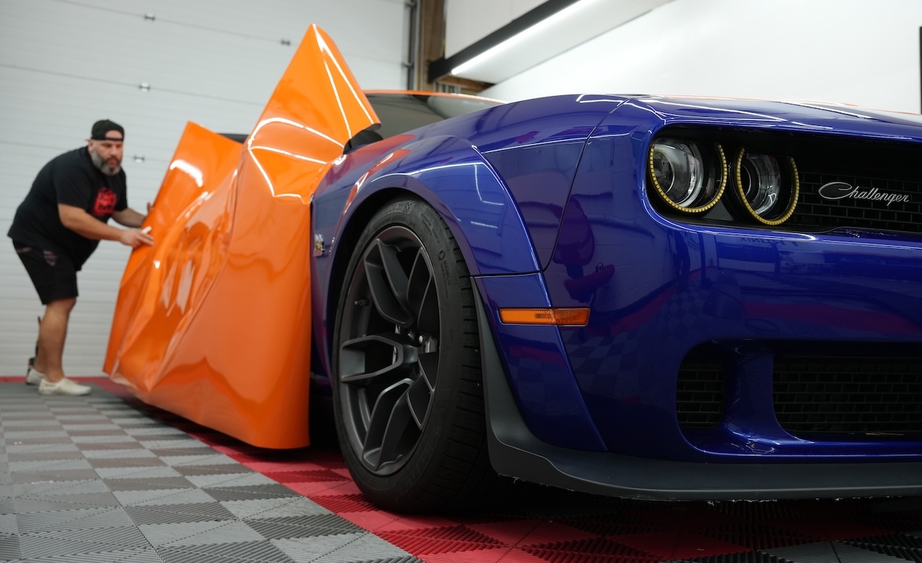 Prime Graphics Lab employee carefully applying a vinyl wrap to the side of a Dodge Challenger inside the shop.