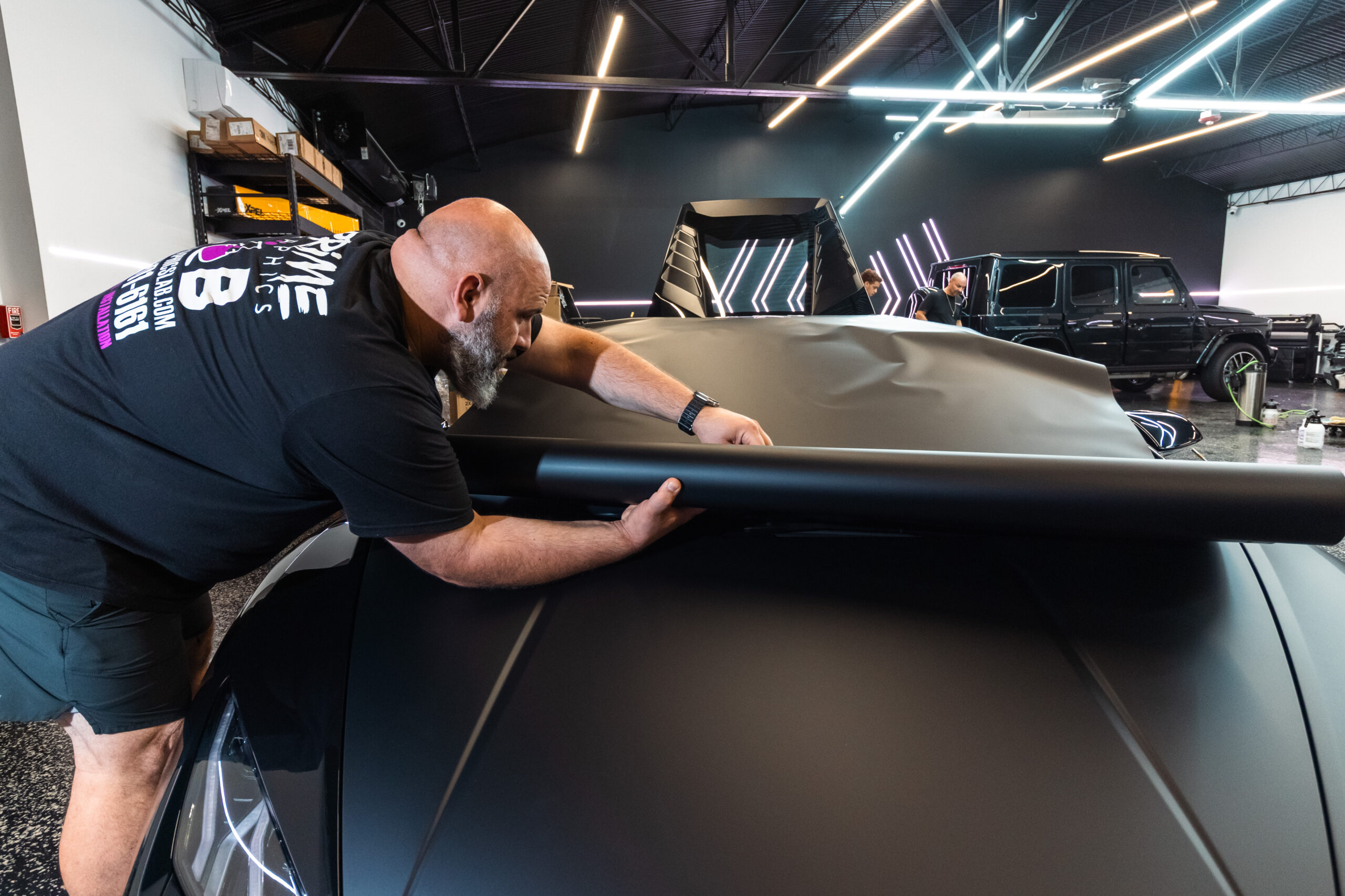 An employee from Prime Graphics Lab carefully applies black satin Dynamic Paint Protection Film (PPF) to a Lamborghini, ensuring a flawless, protective finish.